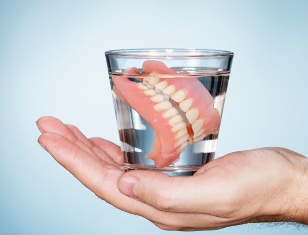 Hand holding glass of water with soaking dentures