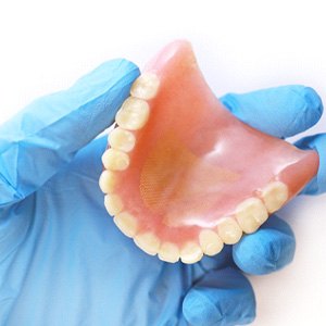 gloved hand holding a full denture