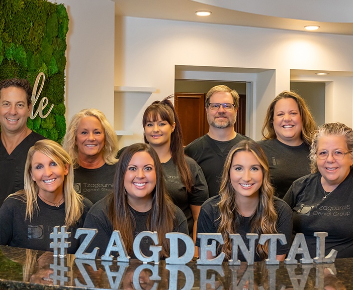 Upper Arlington dental team members behind front desk with sign reading hashtag Zag Dental