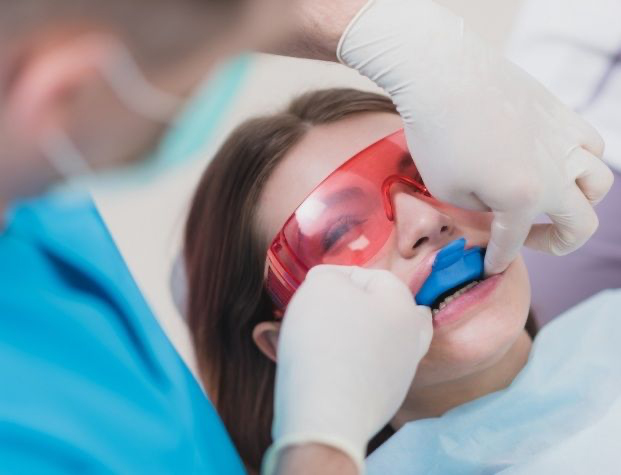 Young woman in dental chair with fluoride treatment trays over her teeth