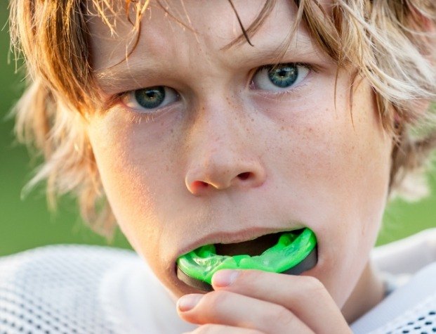 Young boy placing green athletic mouthguard over his teeth