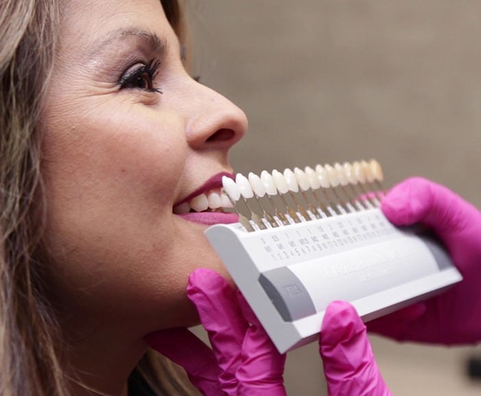 Cosmetic dentist holding shade guide next to a smiling dental patient